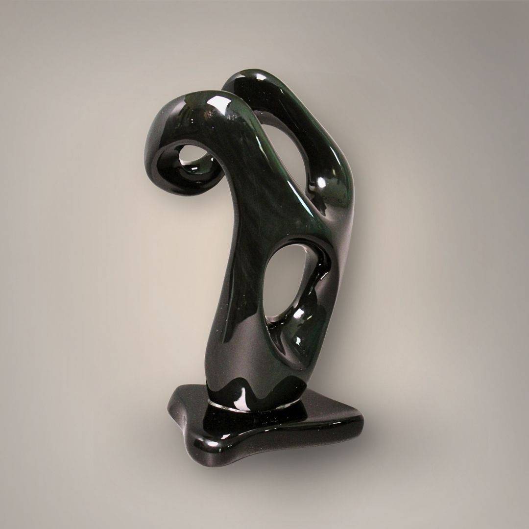 Angled view of polished black and green Velvet Rainbow Obsidian sculpture showing its curved upper section and sculpted openings.