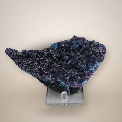 Reverse of Chinese fluorite plate showing irregular pitted surfaces, small cavities, and dark purple and blue mineral zones above a clear display stand.